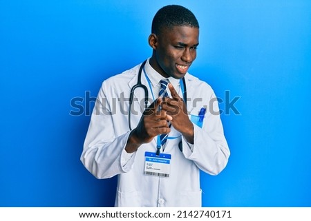 Young african american man wearing doctor uniform pointing fingers to camera with happy and funny face. good energy and vibes. 