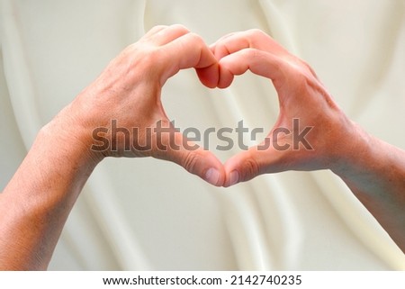 close-up of hands in heart form against white background of silk, concept love, support, mocap for designer