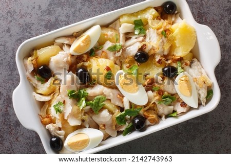 Portuguese Bacalhau a Gomes de Sa salted cod baked with potatoes, onions served with eggs and olives close-up in a baking dish on the table. horizontal top view from above

