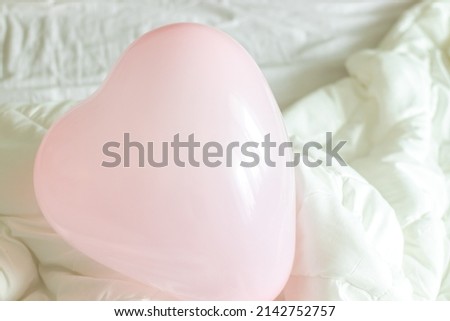pink balloon heart shape on the bed on white blanket or in kid;s hands. happy birthday flags in the background. valentines day concept, or birthday surprise.