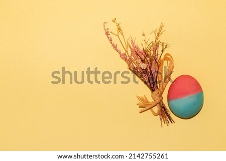 easter pink-blue egg and a small bouquet on a pastel yellow background with lots of copy space, creative holiday concept