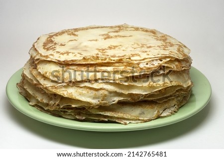 stack of blintzes, greased with butter, traditional product, on green plate, isolated on white background