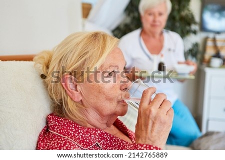 Sick elderly woman takes medication with a glass of water in home care