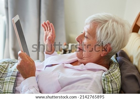 Senior woman in hospital bed video conferencing with family on tablet computer
