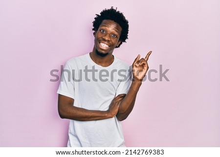 Young african american man wearing casual white t shirt with a big smile on face, pointing with hand and finger to the side looking at the camera. 