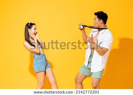 Summer portrait of Asian tourist man taking picture of his girlfriend in studio yellow color background