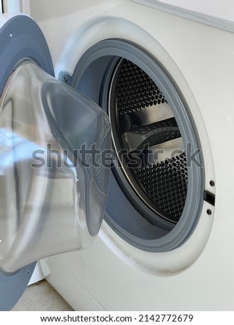 open glass door of a gray steel strip machine drum of a washing machine. front view