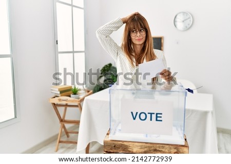 Hispanic business woman voting putting envelop in ballot box confuse and wondering about question. uncertain with doubt, thinking with hand on head. pensive concept. 