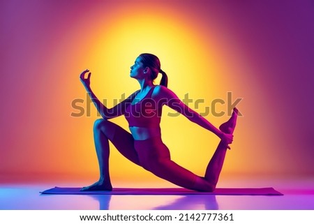 Portrait of young girl training, doing stretching and yoga exercises isolated over gradient pink and yellow background in neon. Sport meditation. Concept of youth, sport, health, fitness, wellness