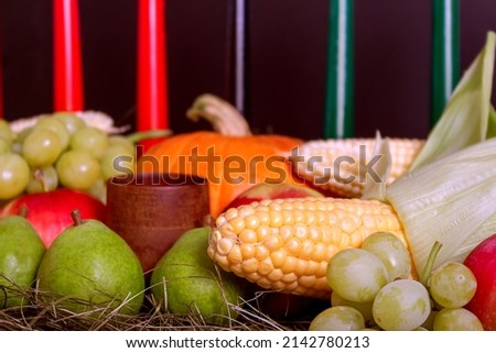 Kwanzaa holiday with candles on black background. Seven candles as symbol of principles of African Heritage. Pumpkin, corn, grapes, pears, apples and wooden bowl. 