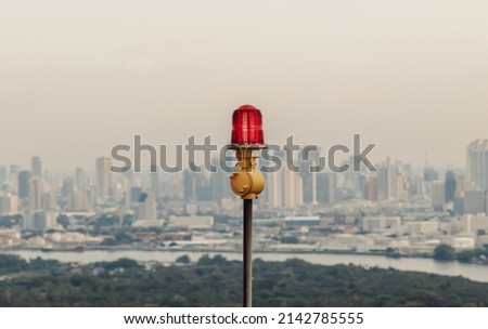 Red lantern of obstruction lights mounted on the rooftop of high rise tall building to ensure flights safety and warn the danger for the plane on the city view background. Red alarm lamp. Royalty-Free Stock Photo #2142785555