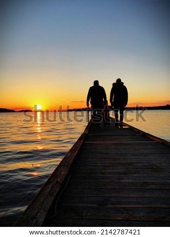 A picture of two parents and a child walking on a jetty at sunset