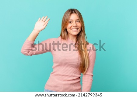 young pretty woman smiling happily, waving hand, welcoming and greeting you Royalty-Free Stock Photo #2142799345