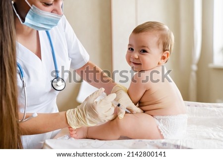 Young female pediatrician or nurse giving an intramuscular injection of a vaccine to leg of little baby boy Immunization for children concept. Happy little cute boy getting a flu shot not afraid of Royalty-Free Stock Photo #2142800141