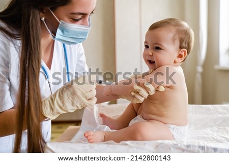 Young female pediatrician or nurse giving an intramuscular injection of a vaccine to hand of little baby boy Immunization for children concept. Happy little cute boy getting a flu shot not afraid of Royalty-Free Stock Photo #2142800143