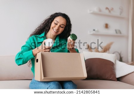 Happy Lady Holding Skincare Cosmetics Products Unpacking Delivered Box After Successful Beauty Shopping Sitting On Couch At Home. Commerce And Delivery Concept Royalty-Free Stock Photo #2142805841