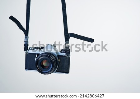 Film photography makes a comeback. Studio shot of a camera hanging by its strap. Royalty-Free Stock Photo #2142806427
