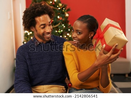 Whatever could it be. Shot of a young woman holding up her Christmas present while sitting beside her boyfriend.