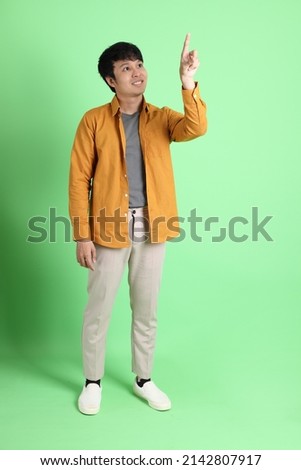 The young adult Asian man with smart casual clothes standing on the light green background.