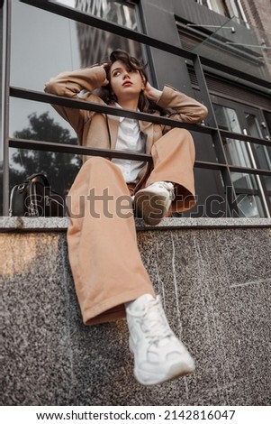  Tall stylish girl with oversized jacket posing near the railing and steps on the city background