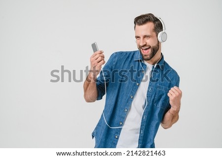 Happy as a winner caucasian young man student freelancer listening to the music in headphones, dancing, choosing sound track on cellphone isolated in white background