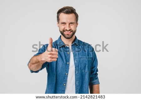 Closeup portrait of positive caucasian young man in denim casual clothes showing thumb up for good quality checkup, smiling with toothy smile isolated in white background Royalty-Free Stock Photo #2142821483