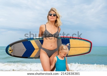 Young adult slim sporty female surfer girl enjoy having fun swimming together with cute little baby girl surfboard ocean coast wave water sunny day. Sport healthy carefree lifestyle vacation concept