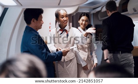 Cheerful black fight attendant and cabin crew assistant checking travel tickets and informing seat to passengers before departure taking care of passengers on airplane working with service mind        Royalty-Free Stock Photo #2142851057