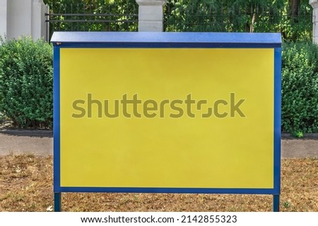 Empty yellow information board with blue frame in city park. Close up advertising display mockup
