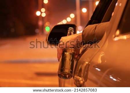 Drunk man driving a car with a bottle of beer at the night. Don't drink and drive concept. Royalty-Free Stock Photo #2142857083