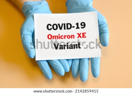 Doctor's hands in blue glove with white paper and text Omicron XE Variant. Concept of medical variety Omicron Variant and COVID-19. COVID-19 Omicron XE Variant concept. Royalty-Free Stock Photo #2142859415