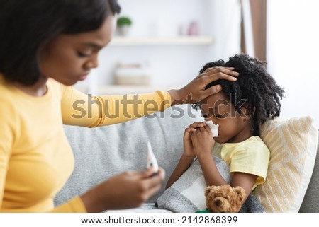 Seasonal Flu Concept. Worried Black Mom Taking Care Of Her Ill Child At Home, Caring Mother Touching Daughter's Forehead And Looking At Thermometer, Checking Kid's Temperature, Closeup Shot Royalty-Free Stock Photo #2142868399