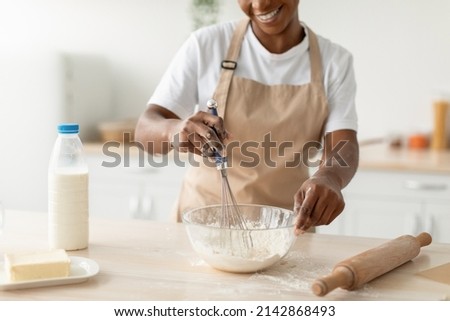 Smiling millennial african american woman in apron preparing dough for pie in minimalist kitchen interior, cropped. Housewife cook at home, health care and food blog at home during covid-19 quarantine Royalty-Free Stock Photo #2142868493