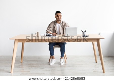 Smiling Middle Eastern Male Manager Working On Laptop Computer In Modern Office, Cheerful Guy Sitting At Desk And Using Pc, Looking At Screen Typing On Keyboard, Enjoying Remote Job, Full Body Length Royalty-Free Stock Photo #2142868583