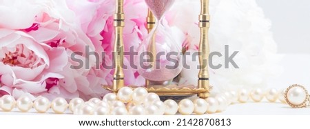 Vintage hour glass, pearls and fresh peony flowers on white leather background