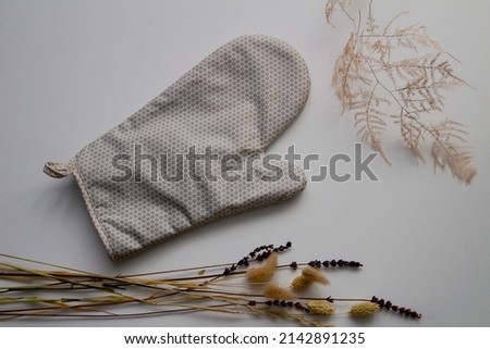 Grey kitchen mitten, golden thin branch and herbarium of lavender, lagurus and phalaris flowers on a gray background. Top view. 