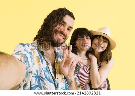 Group of three friends taking selfie with smart phone on studio with yellow background