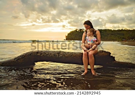 A happy family at the beach a mother child daughter having fun at sunset sit on tree