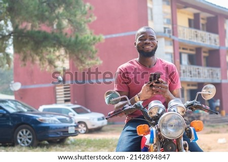 african bike rider smiling and holding his phone Royalty-Free Stock Photo #2142894847
