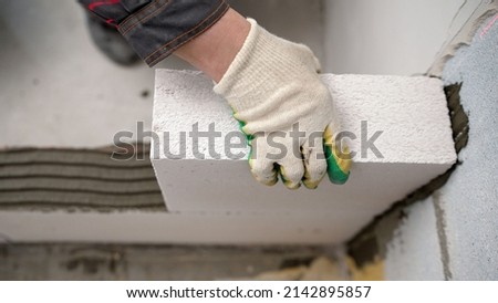The master lays a wall of blocks. Builder builds a concrete wall made of cement blocks on the construction site of a residential building with his own hands. Concept of building a house.  Royalty-Free Stock Photo #2142895857