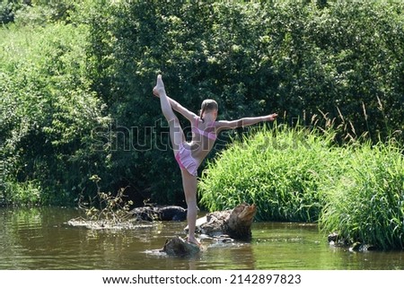The girl does exercises on the river in landscape. Yoga kids