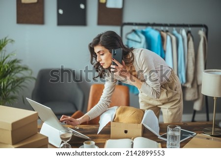 Working woman in an online store. She wears casual clothes and checks the customer's address and package information on the laptop. Online shopping concept Royalty-Free Stock Photo #2142899553