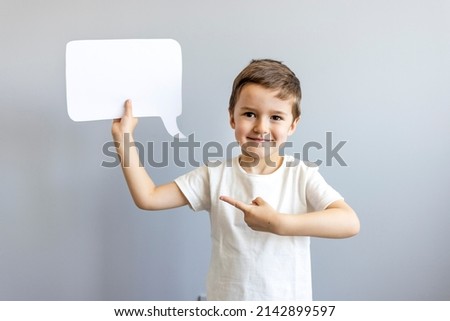 Studio portrait of a happy boy with a clean white board in the shape of a cloud on a bright gray background, with a place for your text or advertising