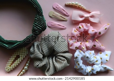 Colorful scrunchies, emerald green headband and pearl hair clips on pastel pink background. Flat lay.
