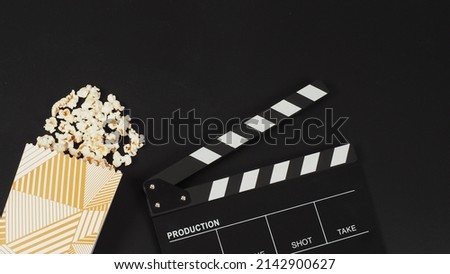 Black clapper board or movie slate and a white box of popcorn on black background.	

