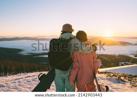 Snowboarders couple enjoying sunset in ski resort beautiful mountains