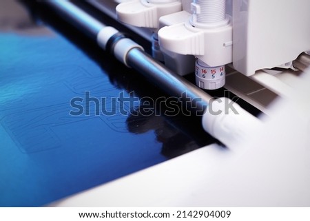 plotting machine cuts high detailed tiger striped lettering from black adhesive foil in blue dazzling light. selective focus. advertisment and individualization concept