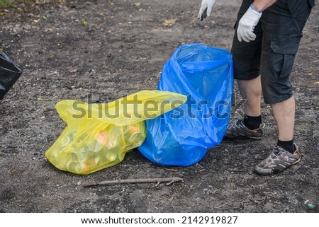 woman sorts garbage in yellow and blue bags on the nature