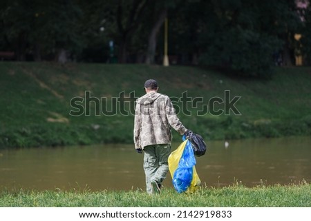 man collects garbage in nature near the river