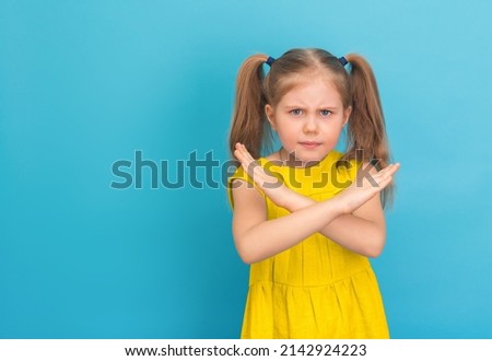 Little girl in yellow dress with negative expression on fer face showing stop gesture on blue background.